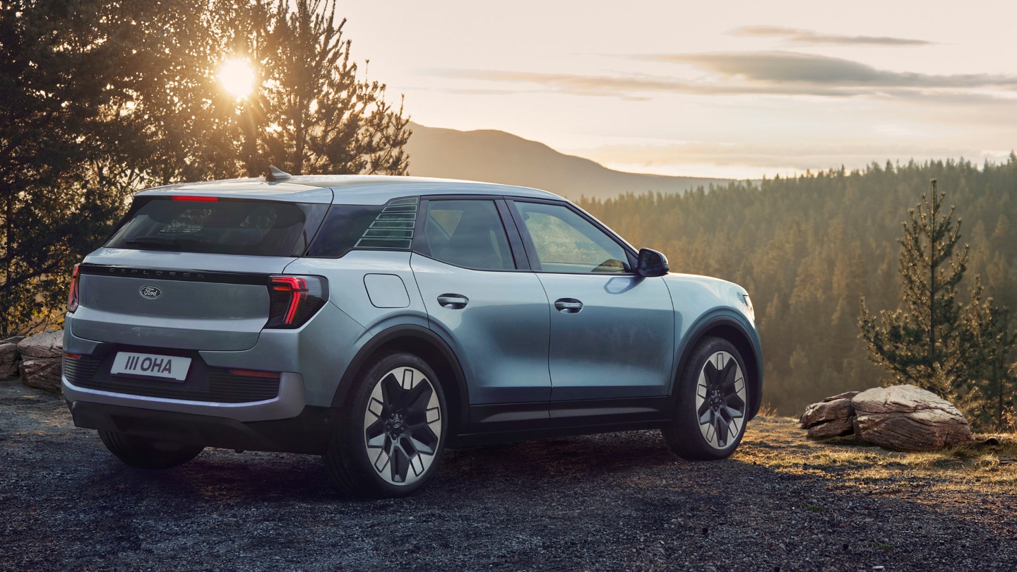 Rear view of a silver Ford Explorer parked on a hill, with a mountain range and sunset in the background.