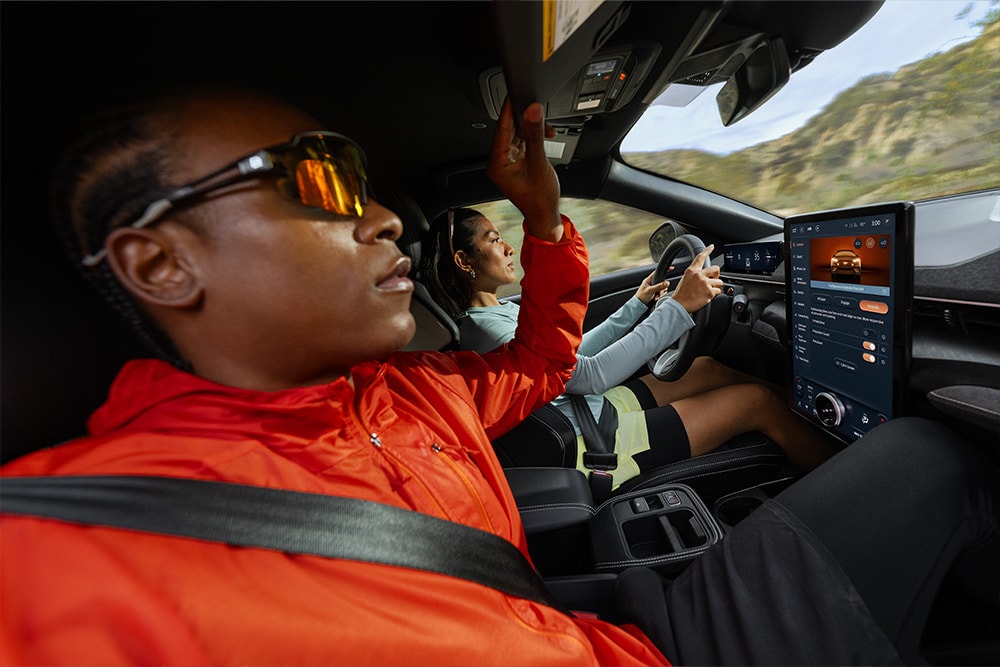 A person sits in the passenger seat of a Ford Mustang Mach-E beside the driver display screen.