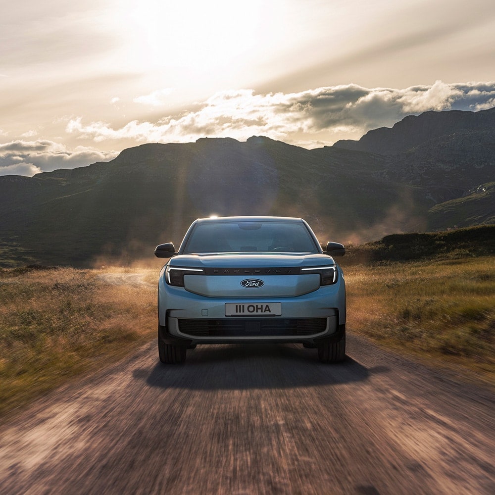 A light blue Ford Explorer driving on a dirt road in a mountainous landscape.