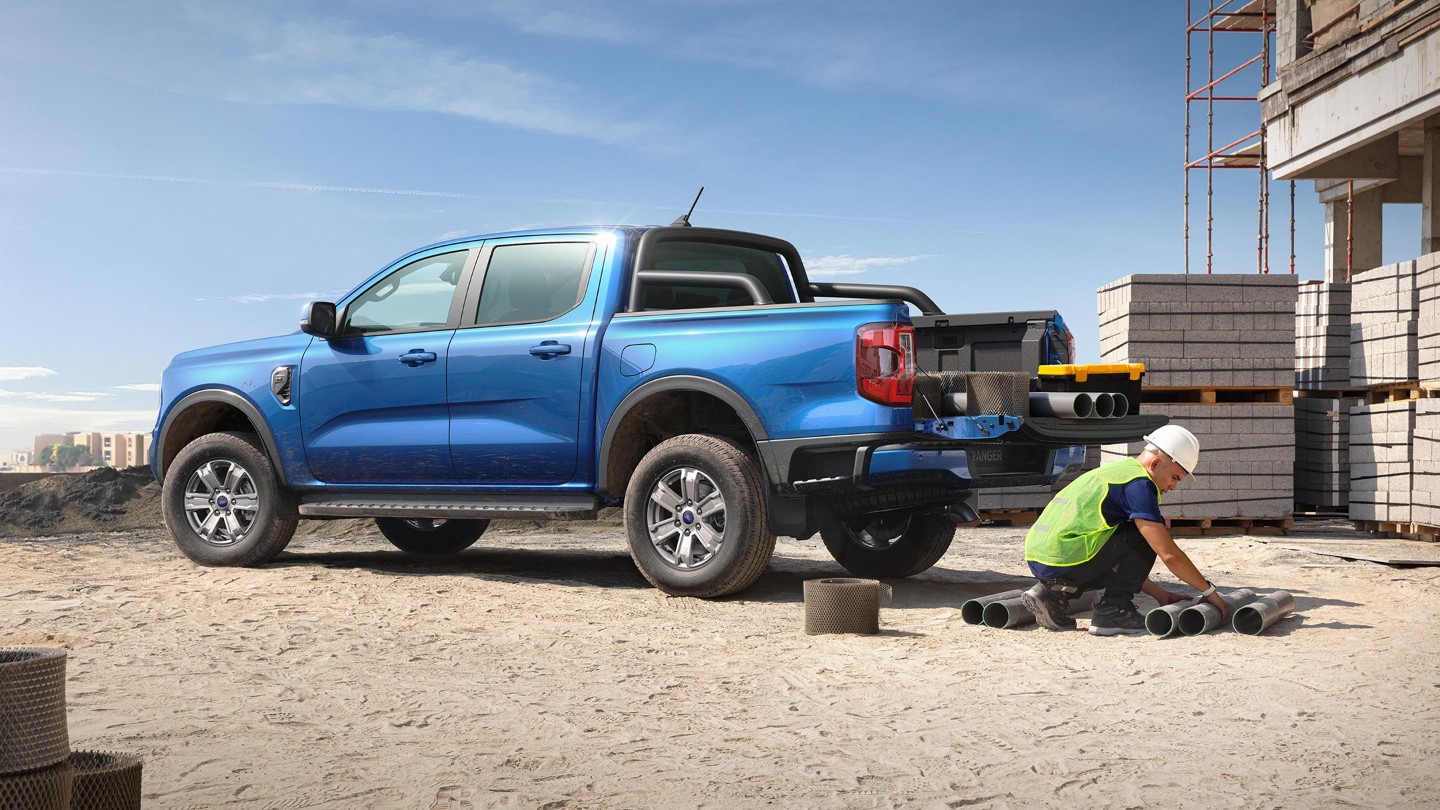Blue Ford Ranger pickup truck at a construction site, with a worker handling pipes near building materials.