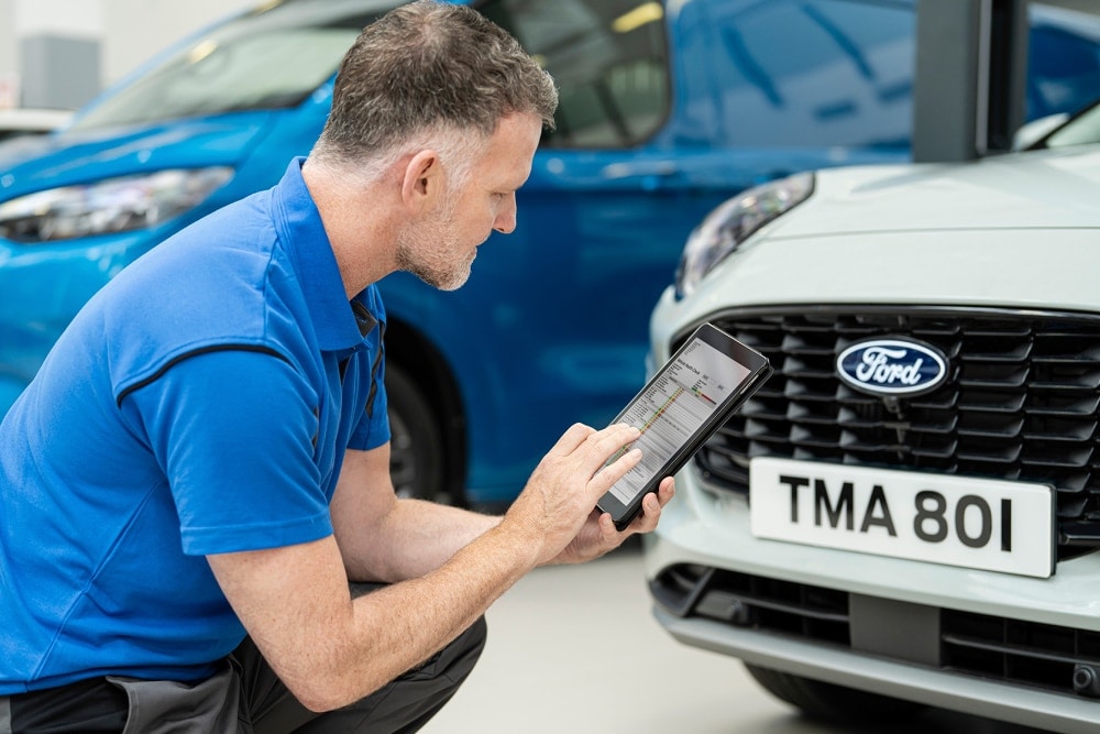 A technician kneels beside a Ford Puma, checking details on a handheld tablet near the front grille.