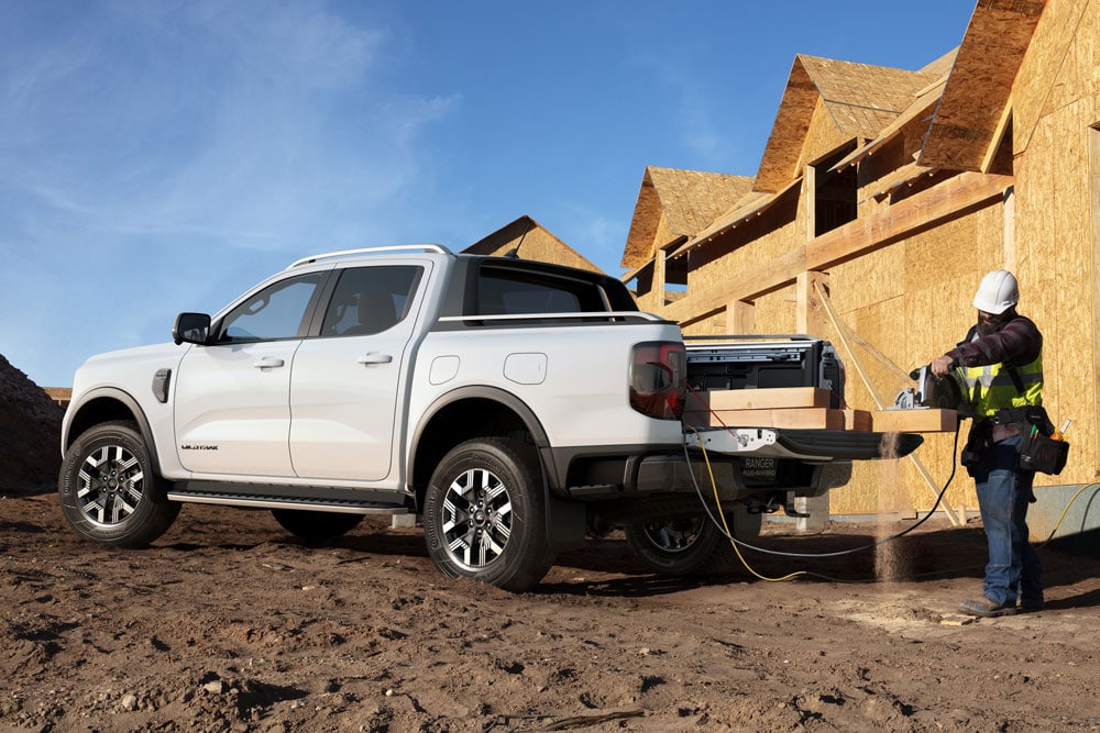 A white Ford Ranger PHEV on a construction site where wood is being chopped in the rear bed using Ford Pro Power Onboard.