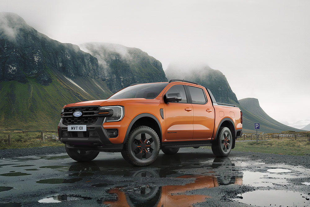 An orange Ford Ranger in a car park at the bottom of a mountain.