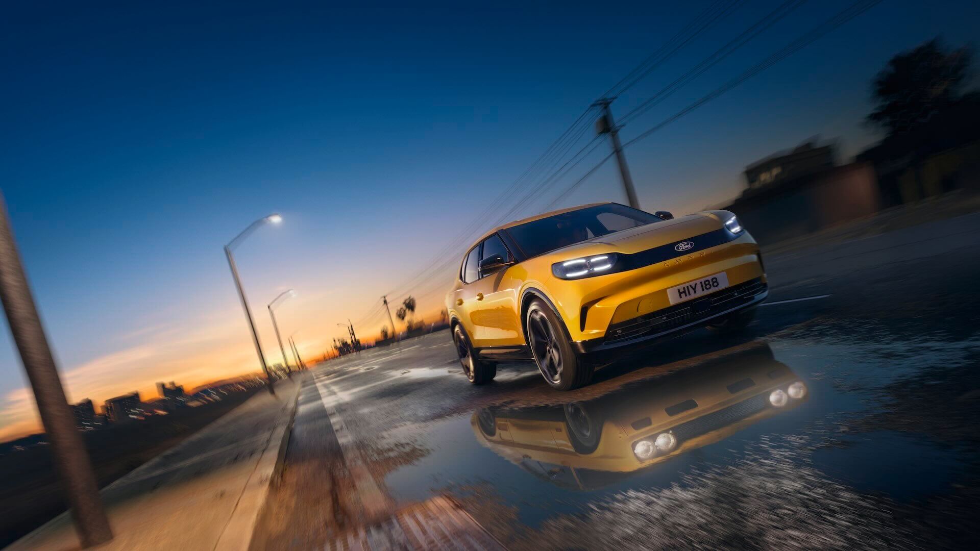 Front view of a yellow Ford Capri on a wet road, with a reflection of the original Capri model.