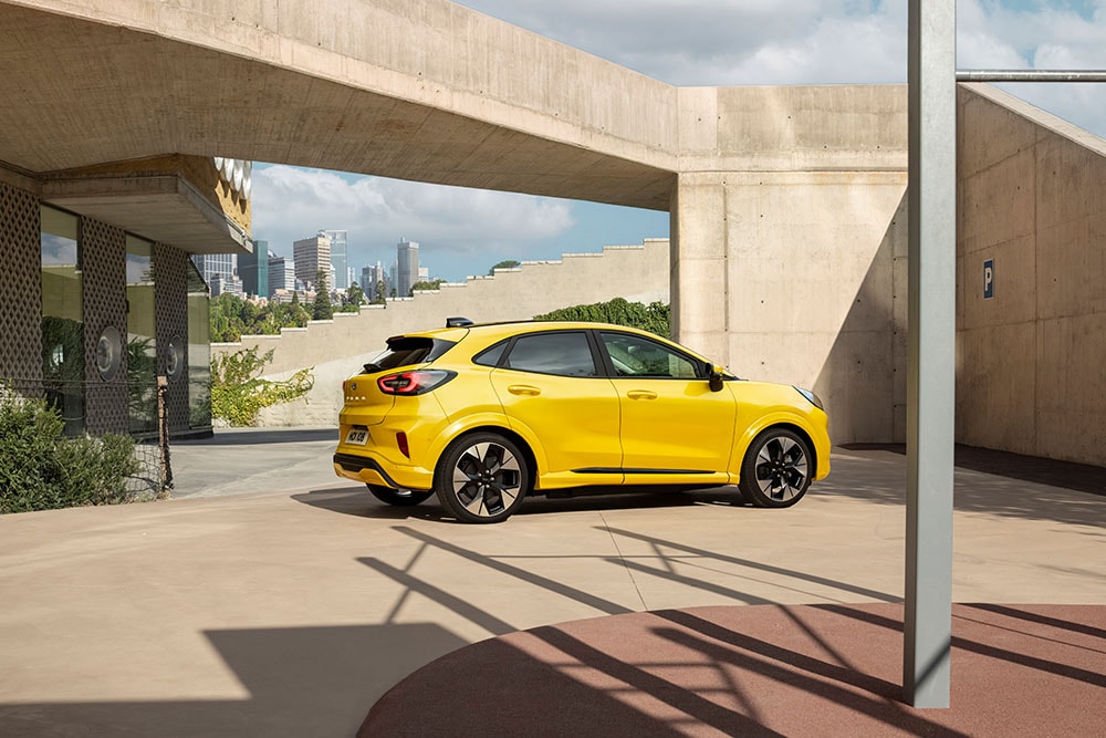 Side view of a yellow Ford Puma Gen-E parked in an urban environment.