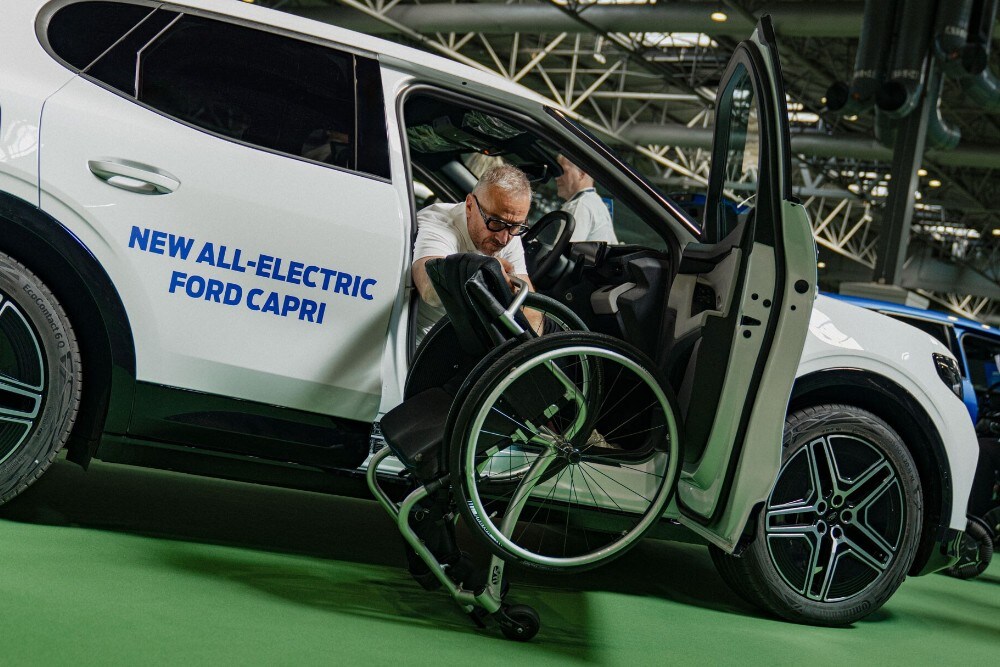 Jason Richards in a wheelchair next to a white Ford Capri with "NEW ALL-ELECTRIC FORD CAPRI" on the side.