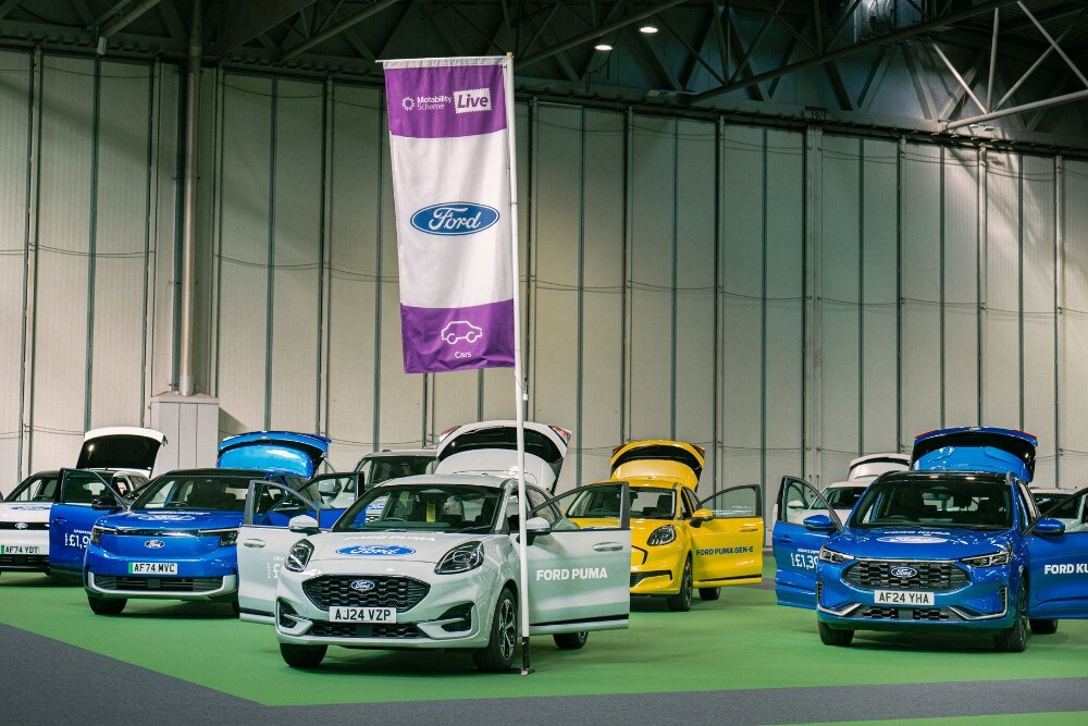 Ford vehicles (Puma, Kuga, Capri, Explorer, Gen-E) and a Ford flag at an event with open doors.