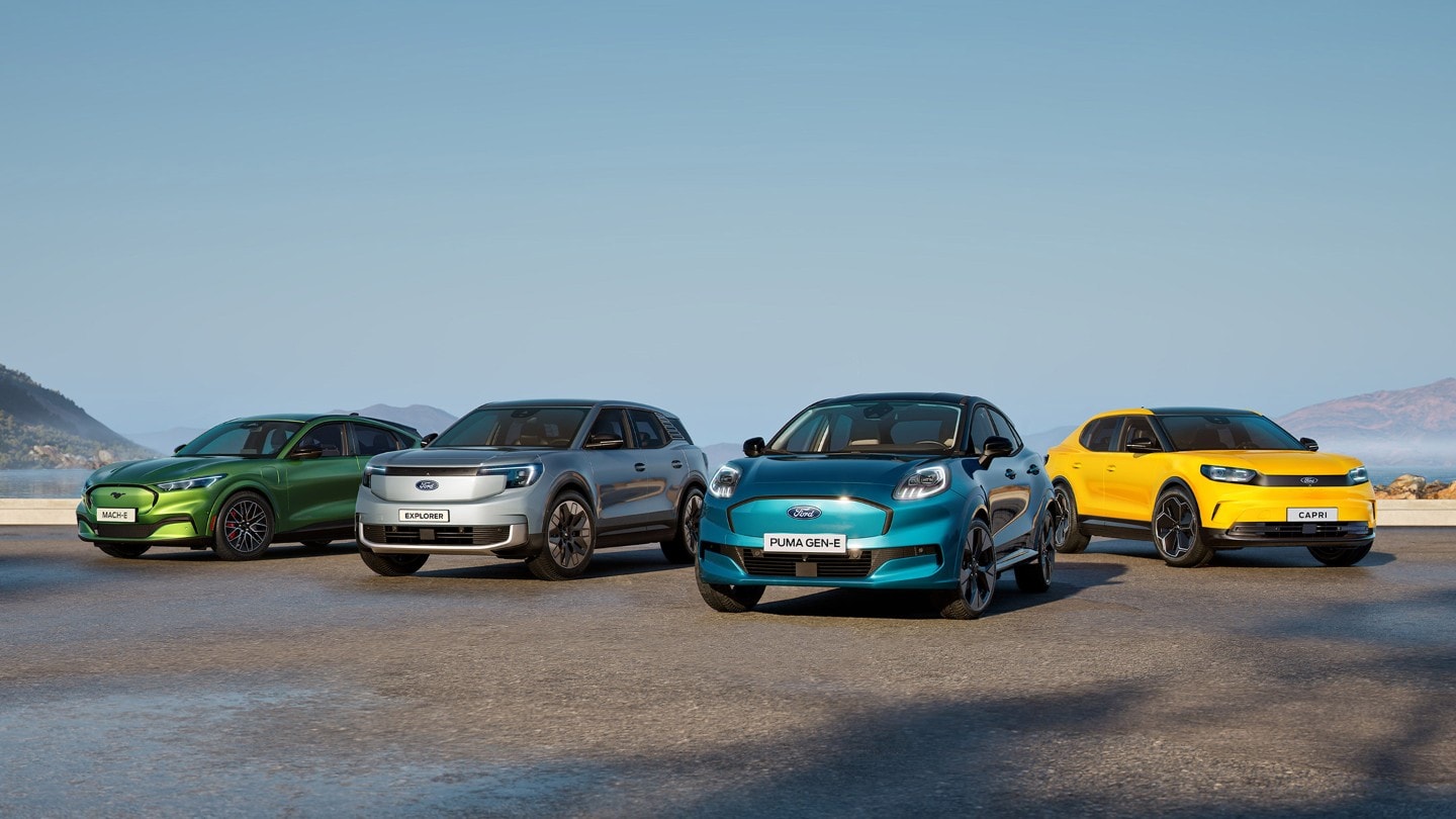 Four Ford electric vehicles: green Mach-E, silver Explorer, teal Puma Gen-E, and yellow Capri, on a coastal road.