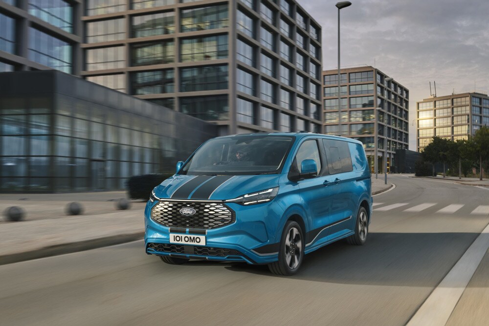Blue Ford E-Transit Custom with black stripes driving on a city street.